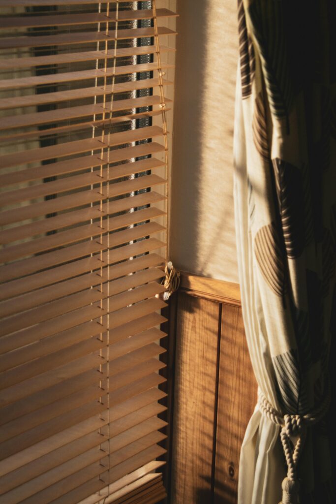 Cozy indoors scene of sunlight casting shadows through blinds and curtains.